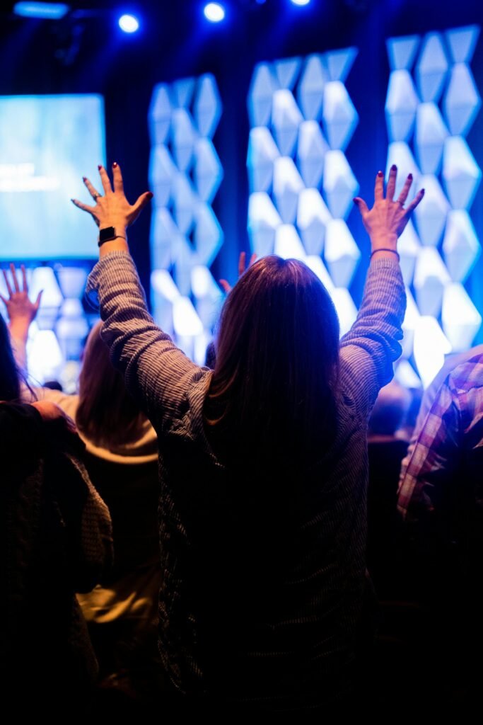 A woman raising her hands in worship during a vibrant indoor event with blue lighting.