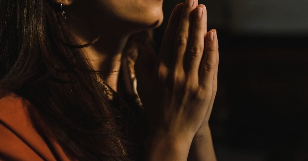 Close-up of a woman with folded hands praying, captured in a serene indoor setting with low lighting.